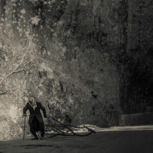 Oeuvre d'art réalisée en 2015. Cette photo nous présente la marche d'un vieil homme, trainant une branche d'arbre, devant une falaise, dans un village syrien.