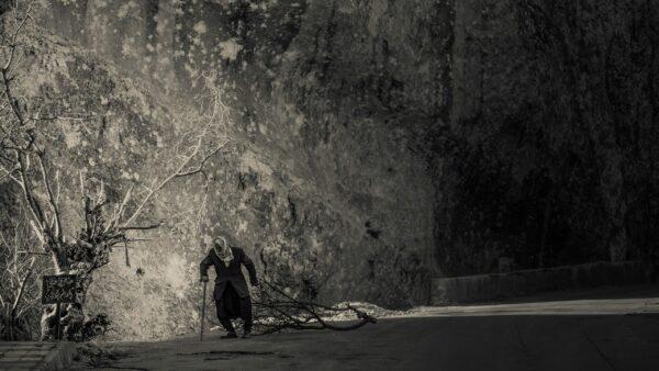 Oeuvre d'art réalisée en 2015. Cette photo nous présente la marche d'un vieil homme, trainant une branche d'arbre, devant une falaise, dans un village syrien.
